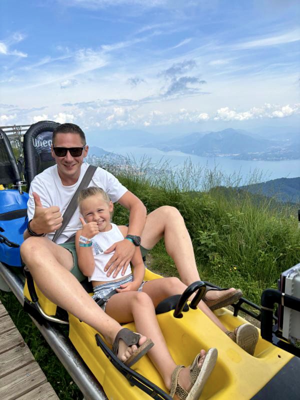 Foto di un papà con una bambina seduti sul bob di alpyland mottarone fun bob con vista sul lago laggiore nel comune di stresa